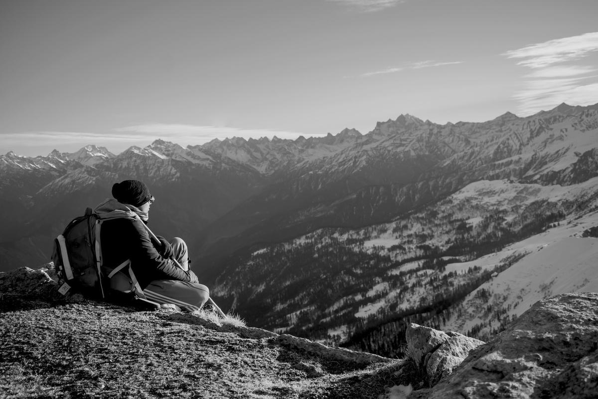A hiker resting on a ridge above a snow-covered mountain range